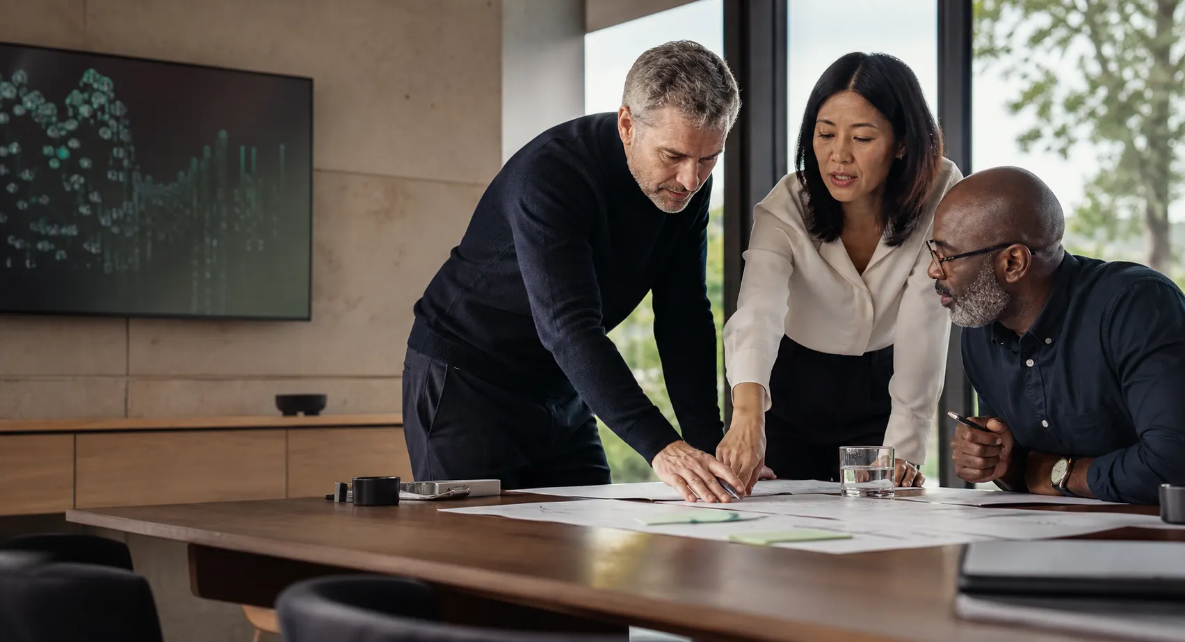 Three experienced business and technology professionals collaborating around a shared table in a modern workshop room.